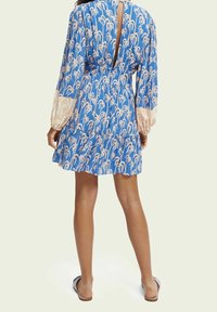 Modré šaty s vzorem a dlouhými rukávy, s výřezem ve tvaru klíče na zádech a splývavou sukni zdobenou růžovými květinovými motivy.