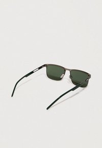 Gafas de sol rectangulares con lentes verdes oscuros. Las monturas están hechas de un material marrón mate. Las varillas son verdes brillantes con acentos plateados.