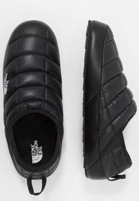 Black insulated slip-on shoes with a quilted design, rubber sole, and pull tab at heel. Features logo on the side. Lightweight construction.
