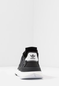 Svart och vit Adidas-sneaker sedd bakifrån, med mesh- och syntetiska material samt en strukturerad vit sula.