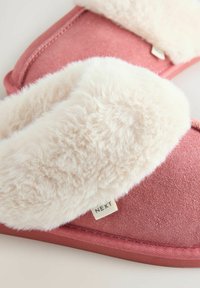 Pink slippers made of soft fabric with a fluffy white faux fur cuff. Features a small "NEXT" label on the side. Flat, rounded shape.