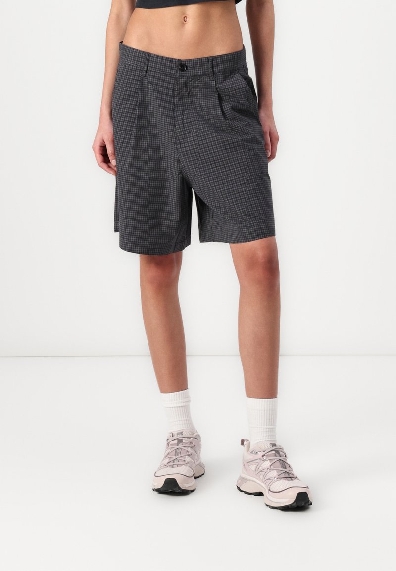Gray checkered shorts with a relaxed fit, featuring a waistband and side pockets. Styled with pink athletic shoes and white socks.