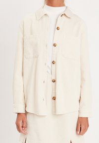 Krämmad kordjacka med två bröstfickor, bruna knappar och krage. Strukturerad tyg och avslappnad passform.