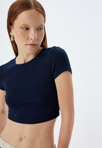 Marineblå crop top i et tætsiddende design, lavet af glat stof med korte ærmer og rund halsudskæring. Fremhævet af minimale syninger.
