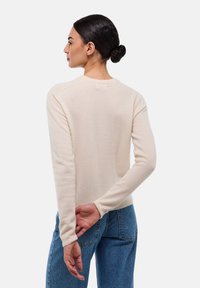 Pull en tricot beige avec des manches longues, un col rond et des poignets côtelés. Associé à un jean bleu, présenté de dos, en mettant l'accent sur la texture.
