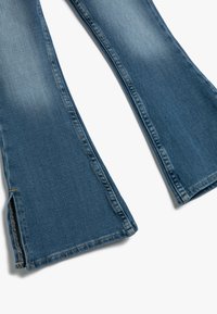 Blå denimflares med en blekt finish, med sidöppningar och synlig sömnad. Kapade vid ankellängd, med en lätt texturerad yta.