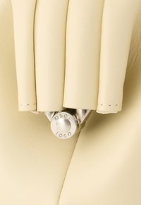 Κοντινό πλάνο επίπλωσης από εκρού δέρμα με ένα γυαλιστερό μεταλλικό κουμπί με ανάγλυφο το γράμμα "OSOI" που συγκρατεί διπλωμένες στρώσεις δέρματος.