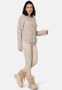 Hellbeige gestrickter Pullover mit bunten Sprenkeln, kombiniert mit engen beigen Hosen und cremefarbenen Stiefeln mit Lammfellfutter. Lässige, entspannte Passform mit seitlichen Schlitzen.