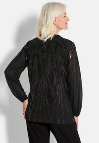Schwarze Bluse mit langen Ärmeln, die ein geometrisches Muster aus Pailletten in Schwarz- und lila-Tönen aufweist, mit lässiger Passform und strukturiertem Stoff.