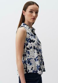 Bezramienna bluzka w kwiaty z kołnierzykiem. Posiada niebiesko-biały wzór kwiatowy na jasnym materiale, zaprojektowana w luźnym kroju.