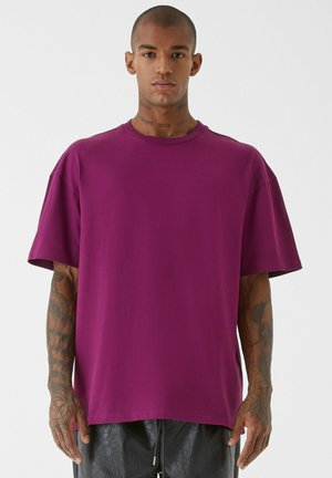 Tricou cu guler rotund și mâneci scurte, dintr-un material violet vibrant. Prezintă o croială lejeră, cu tiv drept și fante laterale. Textură fină.