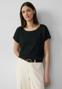 Top negro texturizado de manga corta con escote ancho, combinado con pantalones ajustados color crema y un cinturón negro con herrajes plateados.