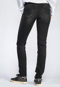 Jeans skinny noirs avec un design à cinq poches, des coutures contrastées et une texture en denim lisse, associés à des baskets noires pailletées.