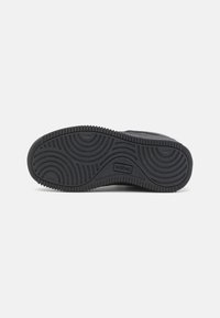 Fekete sneaker talp texturált gumival, körkörös mintákkal és kiemelkedő peremmel; a márka logója látható az oldalon.