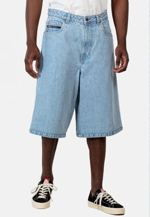 Shorts de mezclilla en azul claro con cintura alta, pierna recta y dobladillo sin terminar. Accentuados con una etiqueta en el bolsillo trasero y combinados con zapatillas negras.