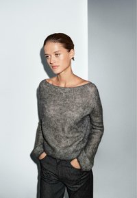 Grå strikket sweater med en bred, off-the-shoulder halsudskæring; har lange ærmer og et blødt, tekstureret stof. Sammen med mørke bukser.
