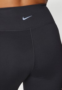 Musta urheilutrikoot, jotka on valmistettu sileästä kankaasta ja joissa on korkea vyötärö. Edessä, lantion alueella, on pieni sininen Nike-logo.