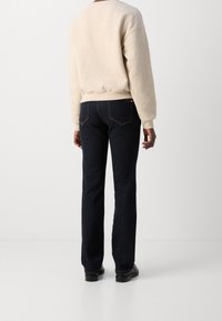 Sudadera beige con hombros caídos, combinada con jeans rectos de color azul oscuro que presentan costuras naranjas y bolsillos traseros. Zapatos negros.