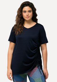 T-shirt blu navy con maniche corte, scollo a V e dettagli arricciati sui lati. Texture morbida, abbinato a leggings a fantasia nei colori vivaci.