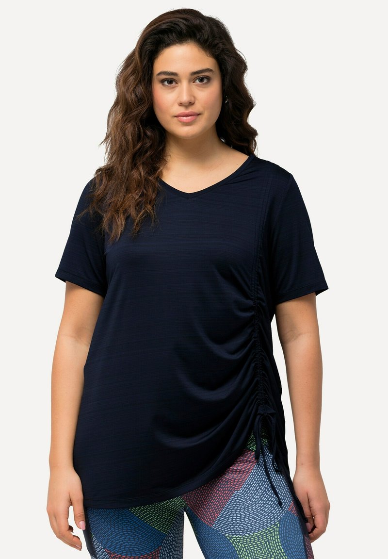 T-shirt blu navy con maniche corte, scollo a V e dettagli arricciati sui lati. Texture morbida, abbinato a leggings a fantasia nei colori vivaci.