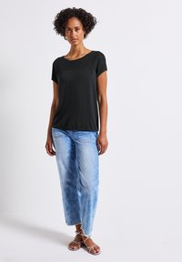 T-shirt noir à manches courtes avec des détails en maille texturée sur le devant, associé à un jean bleu clair à coupe ample et des sandales à lanières.