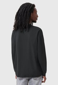 Maglietta nera a maniche lunghe in morbido cotone con una vestibilità rilassata, scollatura rotonda e dettagli di cucitura minimali, abbinata a jeans grigio chiaro.