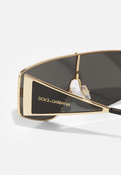 Dolce & Gabbana sunglasses feature a black lens, gold metal frame, and angular design with logo detail on the lens.
