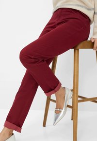Pantaloni bordeaux con orli arrotolati, realizzati in tessuto morbido. Abbinati a scarpe flat argento con una fascia sopra il piede.