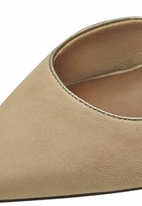 Chaussure en suédine beige à bout pointu avec une finition lisse, présentant un design découpé et un accent métallique fin autour de l'ouverture.
