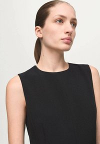 Vestido negro sin mangas con escote alto y textura suave. La tela parece ligera y el diseño es aerodinámico.