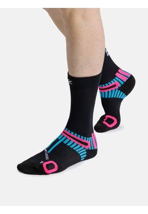 Benen met zwarte sportsokken met felroze en blauwe geometrische accenten, één voet plat en de andere op de tenen.