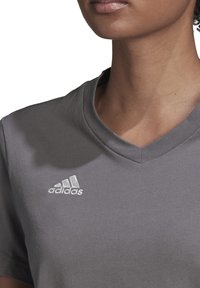 Maglietta girocollo in cotone grigio con maniche corte; presenta il logo Adidas ricamato in bianco sul petto sinistro. Tessuto morbido, vestibilità casual.