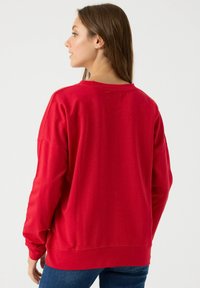 Sudadera roja de gran tamaño con mangas largas, cuello redondo y puños acanalados. Textura suave, dobladillo cosido y corte ligeramente holgado.