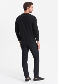 Maglietta nera a maniche lunghe, slim fit, abbinata a jeans scuri e sneaker neri. Tessuto morbido e leggero con collo a giro.