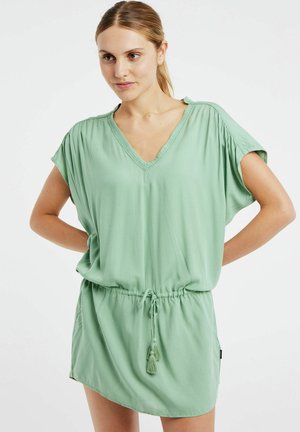 Abito verde chiaro con maniche corte, scollo a V e vita regolabile con lacci. Tessuto morbido, vestibilità casual, presenta un accento con pon-pon sui lacci.