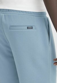Pantaloni de trening de culoare albastru deschis, fabricați dintr-un material moale, având un buzunar la spate cu un eticheta mică. Talie elastică pentru confort.