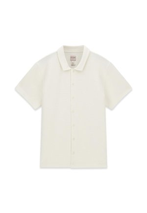 Polo manches courtes, blanc cassé, à boutons, col pointu, tissu texturé et étiquette de la marque Guess à l’intérieur du col.