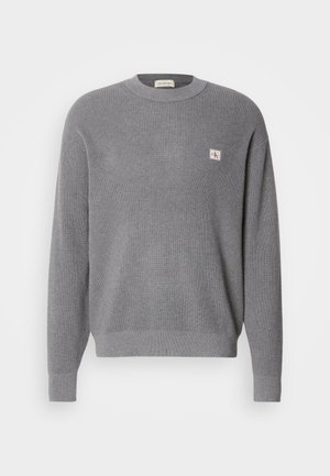 Pullover de malha cinza com mangas longas, textura canelada e um pequeno emblema quadrado CK no lado esquerdo do peito, decote redondo.