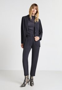 Completo grigio scuro su misura con blazer aderente e pantaloni slim, abbinato a stivaletti alla caviglia in pelle con motivo serpente.