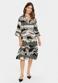 Mustavalkoinen kukkakuosiset mekko, jossa on V-pääntie, kolmannen osuuden hihat ja kerroksellinen hame. Valmistettu kevyestä kankaasta. Mustat kärjet flatsit.