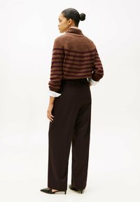 Bruine en bordeaux gestreepte cropped trui met hoge kraag, gecombineerd met zwarte wijde broek en puntige zwarte hakken. Zachte textuur.