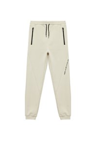 Beżowe joggery wykonane z miękkiego materiału, z czarnymi kieszeniami na zamek i tapered leg, z subtelnymi akcentami po bokach i nadrukowanymi detalami.