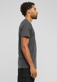 Grå t-skjorte med kort erm i mykt materiale, med rund hals og vanlig passform. Båret sammen med svarte cargo-shorts, vist fra siden.