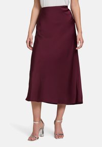 Burgunderfarbene Satin-Midi-Rock mit glatter Textur, hohem Taillendesign und leicht ausgestellter Silhouette. Kombiniert mit silbernen High-Heels.