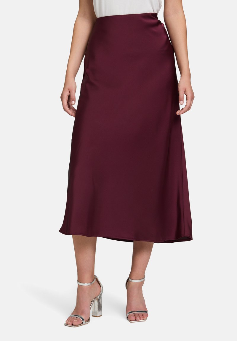 Burgunderfarbene Satin-Midi-Rock mit glatter Textur, hohem Taillendesign und leicht ausgestellter Silhouette. Kombiniert mit silbernen High-Heels.