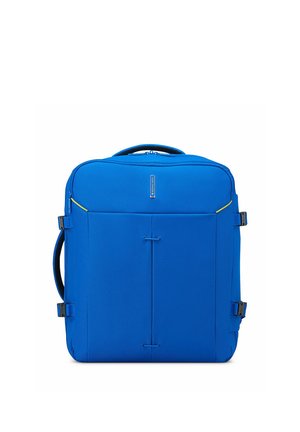Valise souple carrée bleu vif avec poignées latérales, sangles de compression et petite poignée supérieure sur fond blanc.