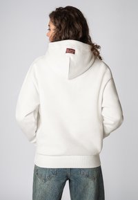 Witte hoodie met een kangoeroezak, ribgebreide boorden en zoom. Heeft een gestructureerde stof en een klein kastanjebruin label op de achterkant van de hals.