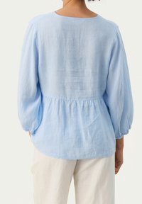 Blusa di cotone azzurro chiaro con vita arricciata, maniche lunghe a sbuffo e scollatura rotonda. Tessuto morbido e design semplice.