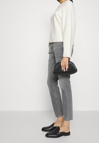 Suéter de manga larga color beige claro, jeans ajustados grises, clutch plisado negro y mocasines negros, con una textura suave y líneas simples.