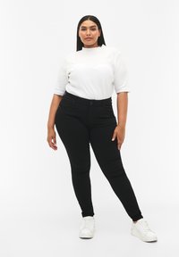 Črne skinny jeans z visokim pasom, z teksturirano površino in petimi žepi, v kombinaciji z belim rebrastim kratkime rokavom.